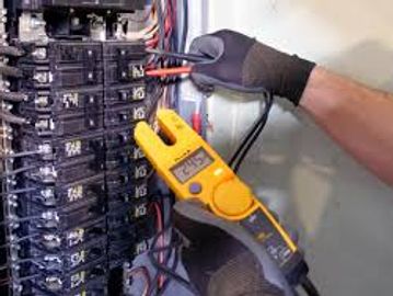 Person using a clamp meter to test electrical current in a circuit breaker panel.