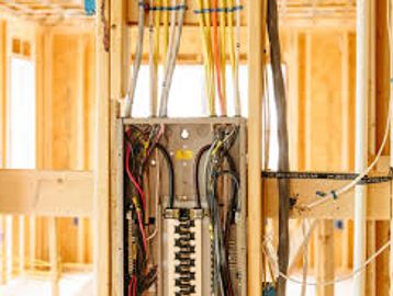 Open electrical panel inside wooden framing of a house under construction.