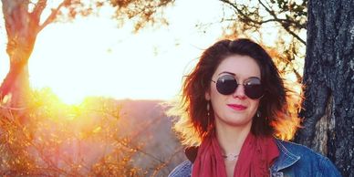 Woman with sunglasses and scarf outdoors at sunset.