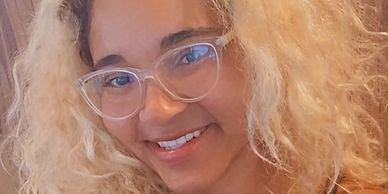 Smiling woman with curly blonde hair and clear glasses.