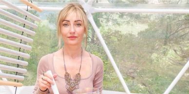 Woman holding a white object inside a bright greenhouse.