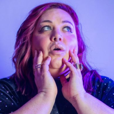 Woman with purple hair in thoughtful pose under blue-purple light.