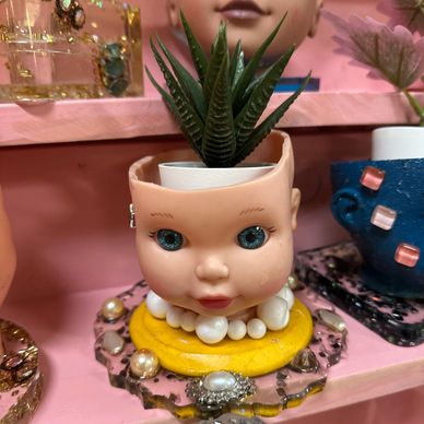 A plant pot made from a doll's head with a succulent inside, surrounded by decorative jewelry.
