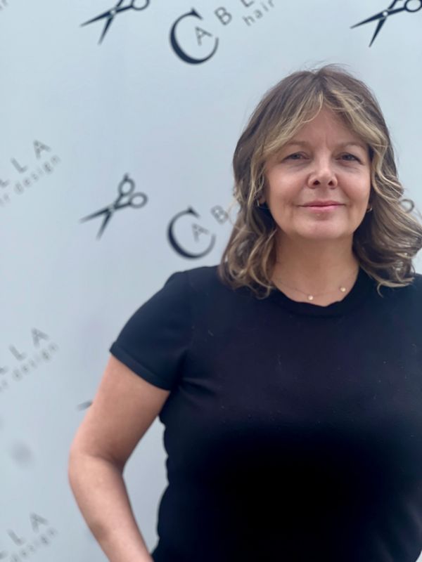 Woman with wavy hair stands in front of a hair design backdrop.