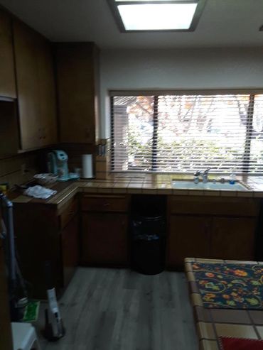 Dimly lit kitchen with wooden cabinets and a window over the sink.