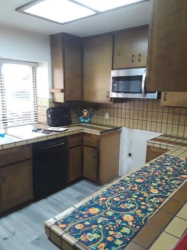 Vintage kitchen with brown cabinets, tiled countertops, and a colorful floral runner.