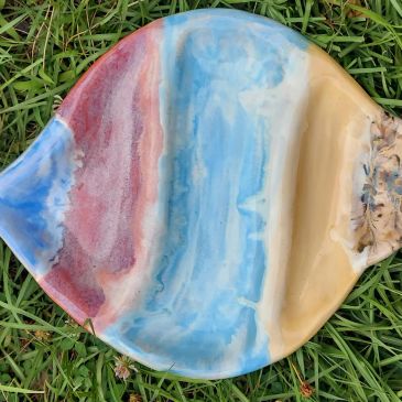 Colorful ceramic fish-shaped plate on grass.