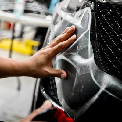 Hand applying protective film on a black car bumper.