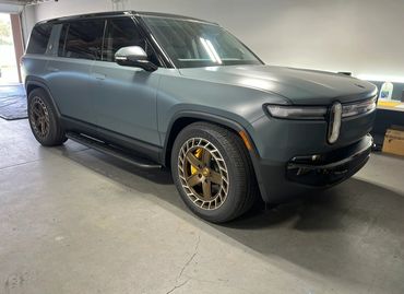 A sleek matte gray electric SUV parked indoors with bronze wheels.