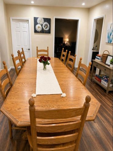 Wooden dining table with chairs and a flower vase in the center.