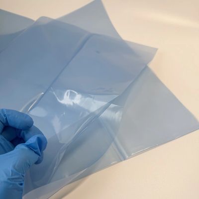 Gloved hand holding a transparent plastic sheet over a blue opaque one on a white surface.