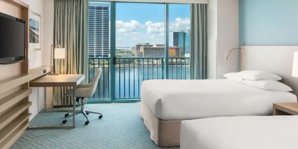 Modern hotel room with two beds and a city view balcony.
