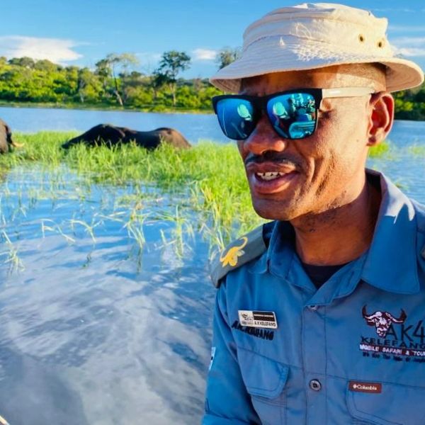 Man in sunglasses and hat near a water body with wildlife.