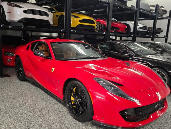 Red Ferrari sports car parked indoors with luxury cars in the background.