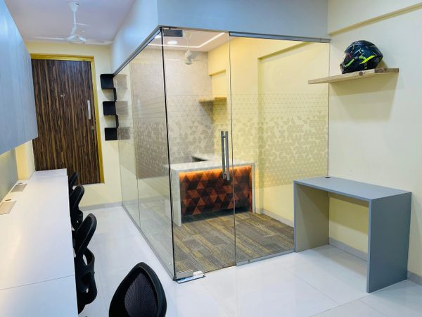 Modern office space with glass partition and ergonomic chairs.