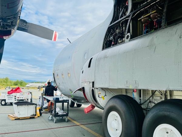 Technicians performing maintenance on a military aircraft on an airport runway.