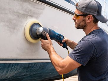 Man polishing a boat hull with a power buffer.