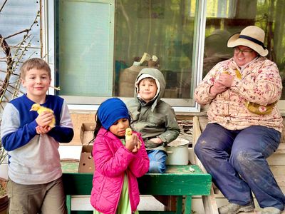 Children and an adult holding yellow chicks outdoors on a porch.