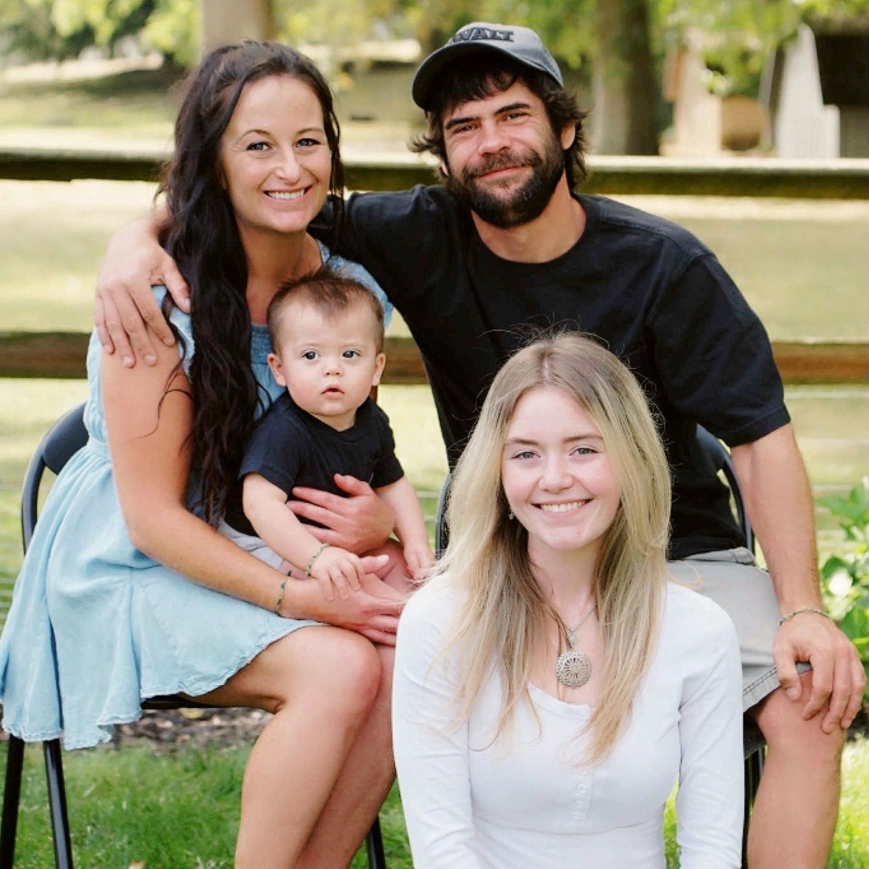 A happy family of four posing outdoors on a sunny day.