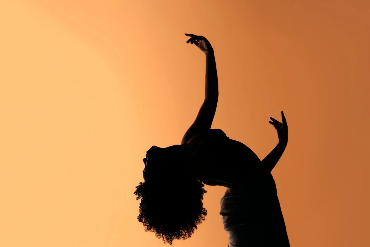 Silhouette of a dancer gracefully arching backward against an orange background.