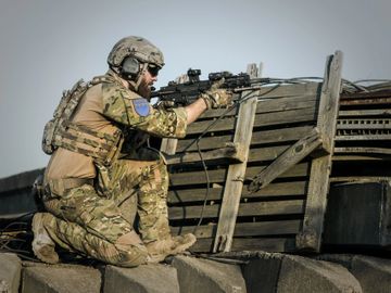 Military member kneeling behind barrier with AR15 carbine rifle, fatigues, protecting his base