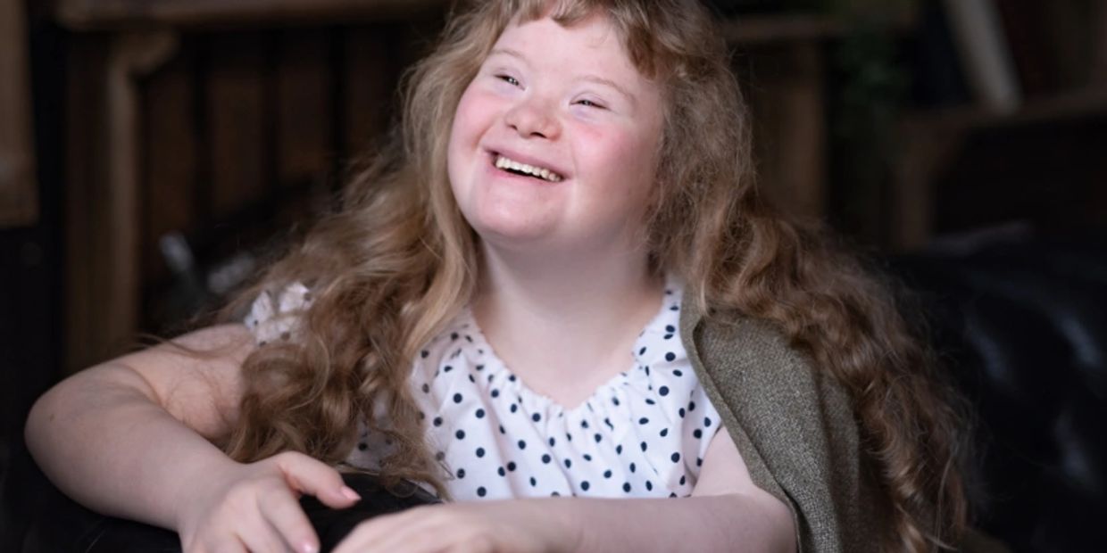 Smiling young girl with long curly hair sitting on a black couch.