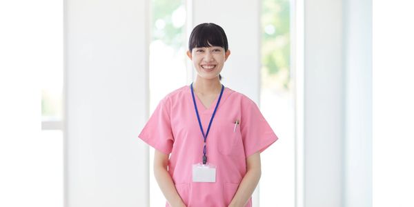 Smiling healthcare worker in pink scrubs with ID badge.