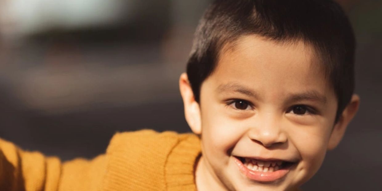 Happy young boy smiling warmly in a cozy mustard sweater.