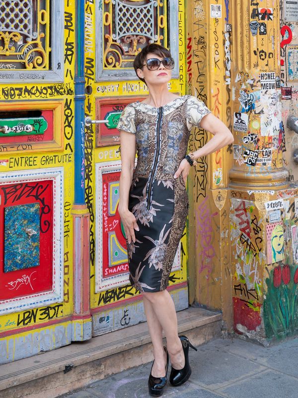 Woman in a stylish dress poses confidently against colorful graffiti-covered doors.