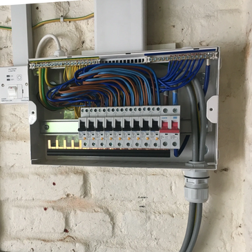 Open electrical panel with organized wiring and circuit breakers mounted on a white brick wall.