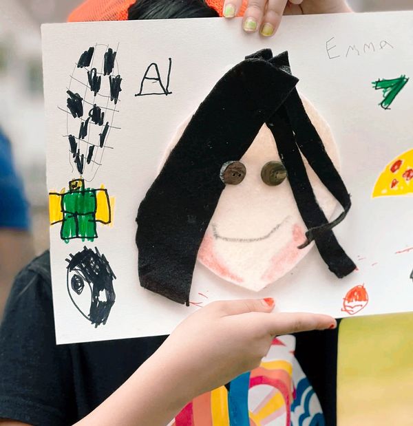 Image of a young hispanic girl holding up a self portrait in front of her face. 