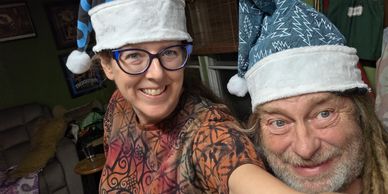 Jess a woman wearing a Santa hat, holding the camera next to Crowley a man wearing a Santa hat