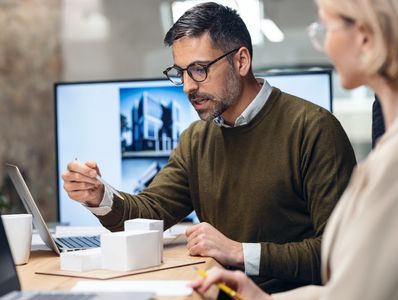 Smart group of architects working with laptops and blueprints while talking of their new design