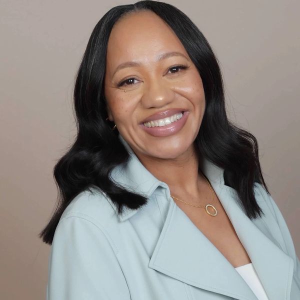 Smiling woman with wavy black hair in light blue blazer.