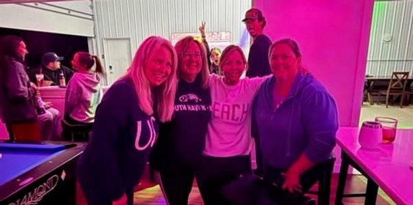 Four women posing at a bar with purple lighting.