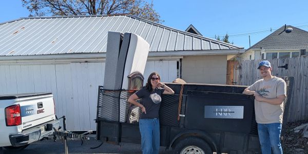 Two people standing by a loaded trailer attached to a white GMC truck.