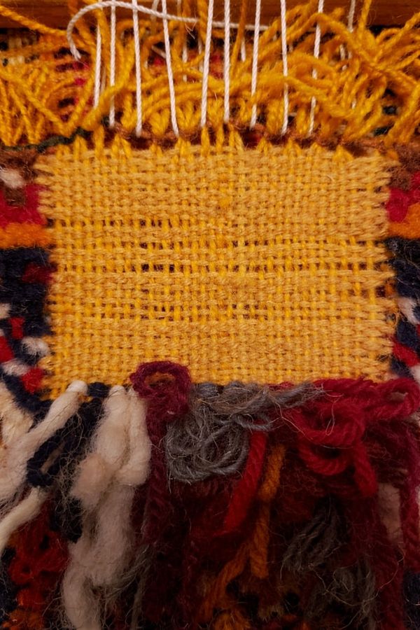 Close-up of yellow woven fabric with multicolored yarn fringes.