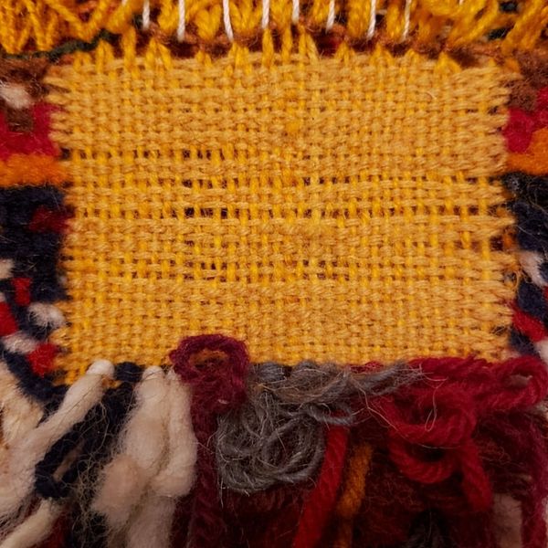 Close-up of a woven textile with yellow threads and colorful yarn fringes.