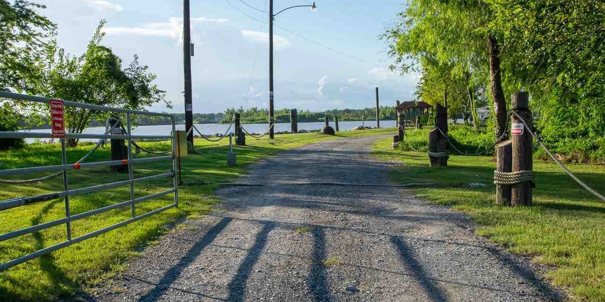 A gravel path leads to a waterfront area with trees and a metal gate.