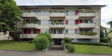 Front view of a residential apartment building with balconies and greenery.