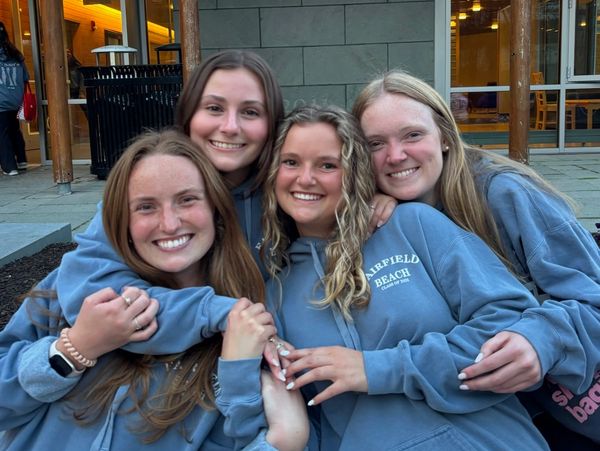 Four friends smiling and hugging, wearing matching blue sweatshirts.