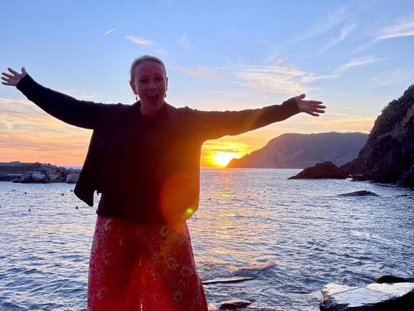 Person enjoying a sunset by the sea with arms wide open.