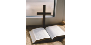 Open Bible with a wooden cross casting shadow on a window sill.