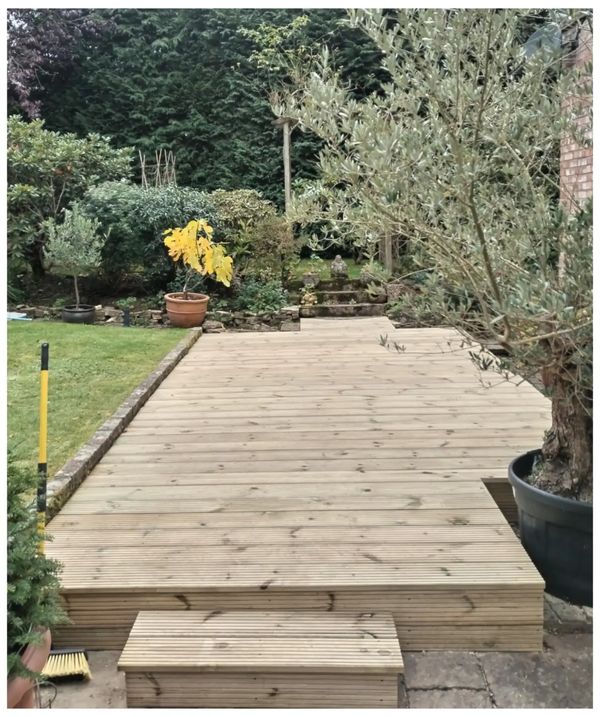 Large decked area in large garden surrounded by a mixture of trees, hedge & plant pots in Newdigate.