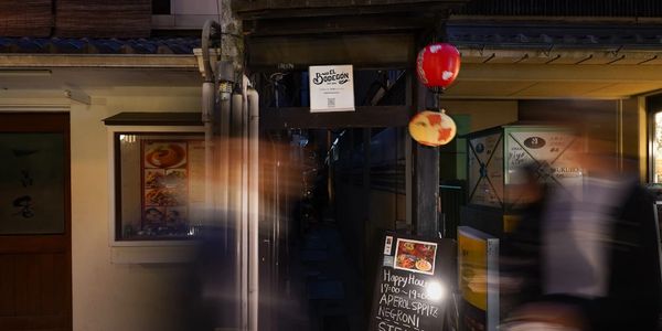 Dimly lit narrow alley entrance off Pontocho with our restaurant sign and blurred pedestrians at night.