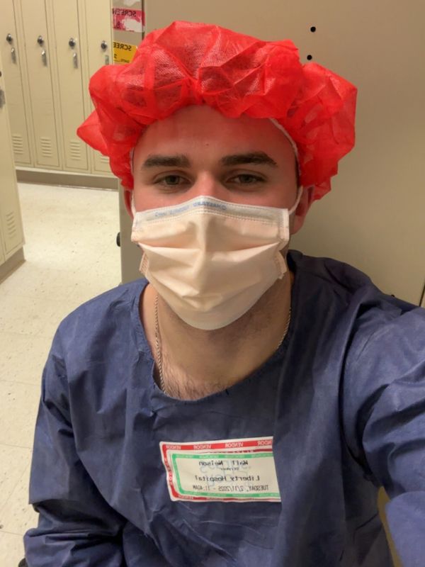 Man in medical scrubs with red hairnet and face mask.