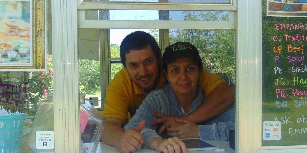 Couple behind a food truck window smiling and posing together.