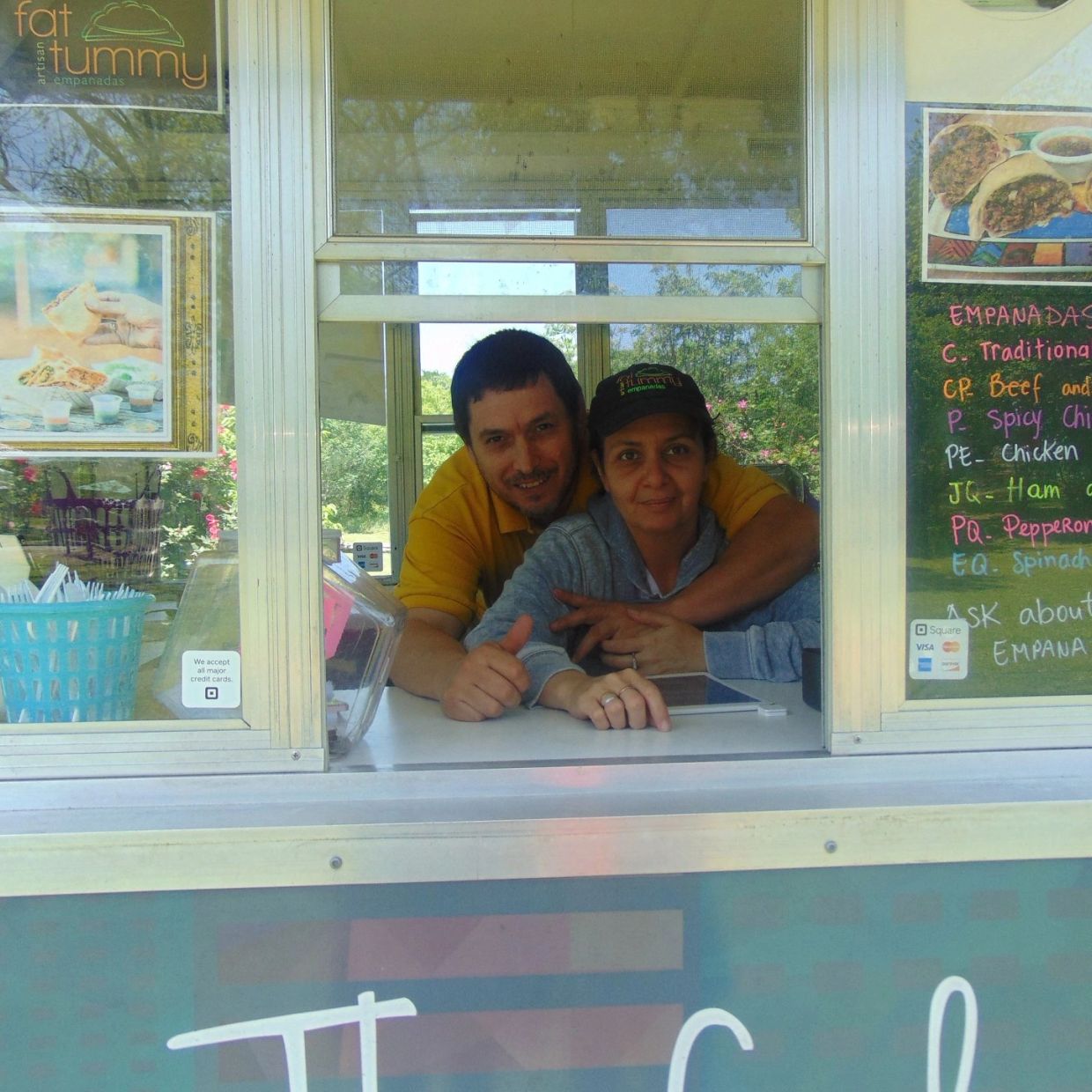 Couple behind a food truck window smiling and posing together.