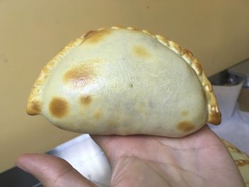 Hand holding a perfectly baked empanada with a golden crust.