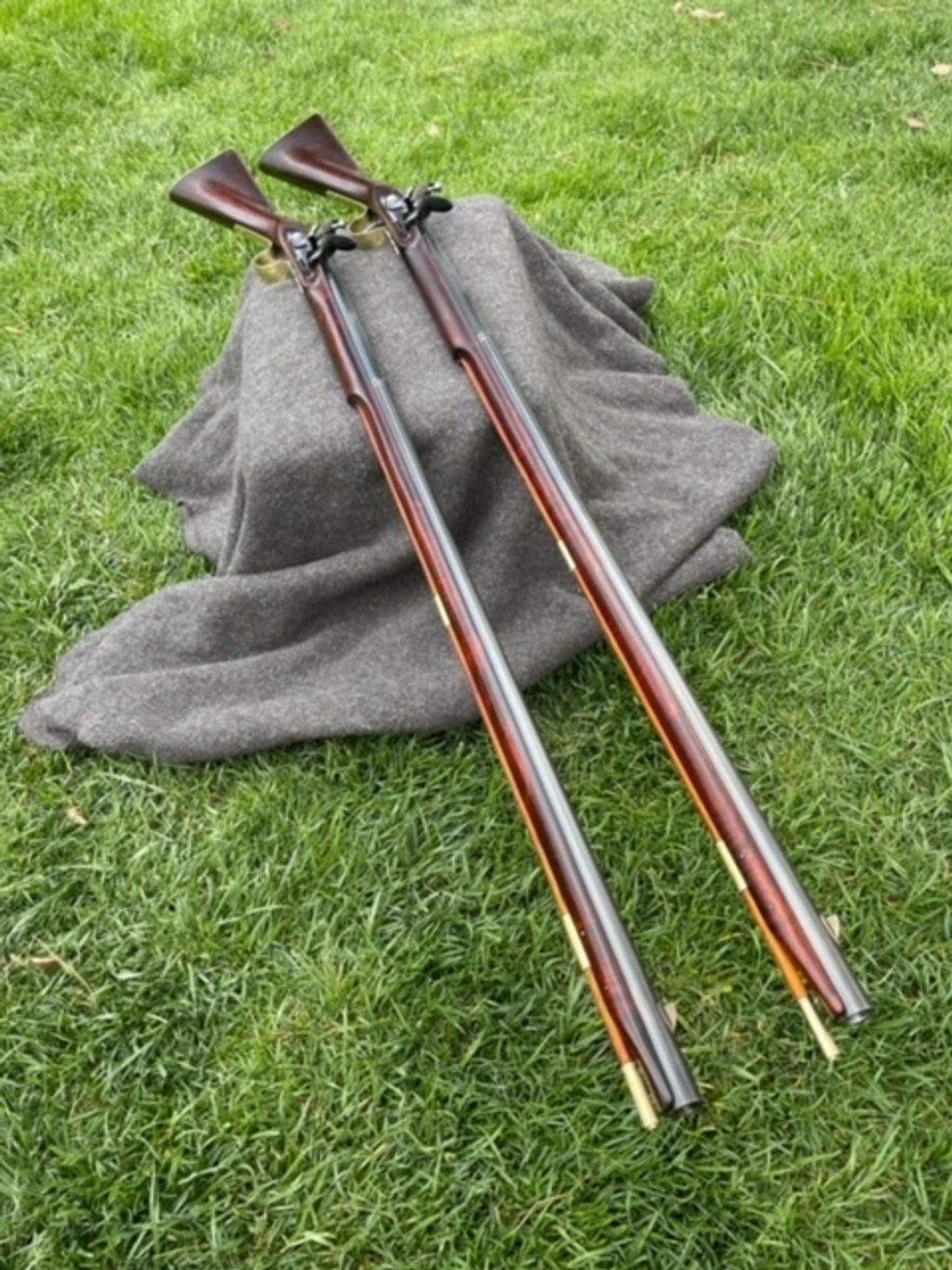 Two antique long rifles displayed on a gray cloth over green grass.